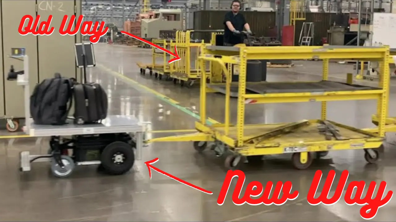 A picture of a Thouzer Giant AGV pulling several yellow carts. Behind Thouzer there's an industrial tugger stopped at the intersection and the operator is smiling at the Thouzer "train."